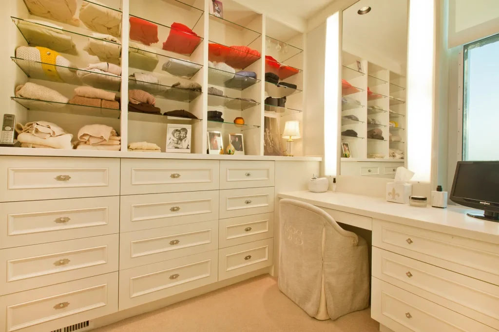 GEORGE dressing-room design with open wardrobes, drawers and a fixed vanity desk with mirror at the end of one wall.
